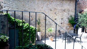 Un pati amb mur de pedra, escala metàl·lica, plantes en testos i mobles d'exterior.