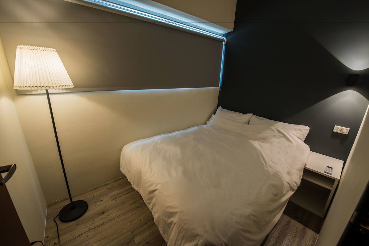 A neatly made bed with white linens in a modern room with a wooden floor and a single bedside table.