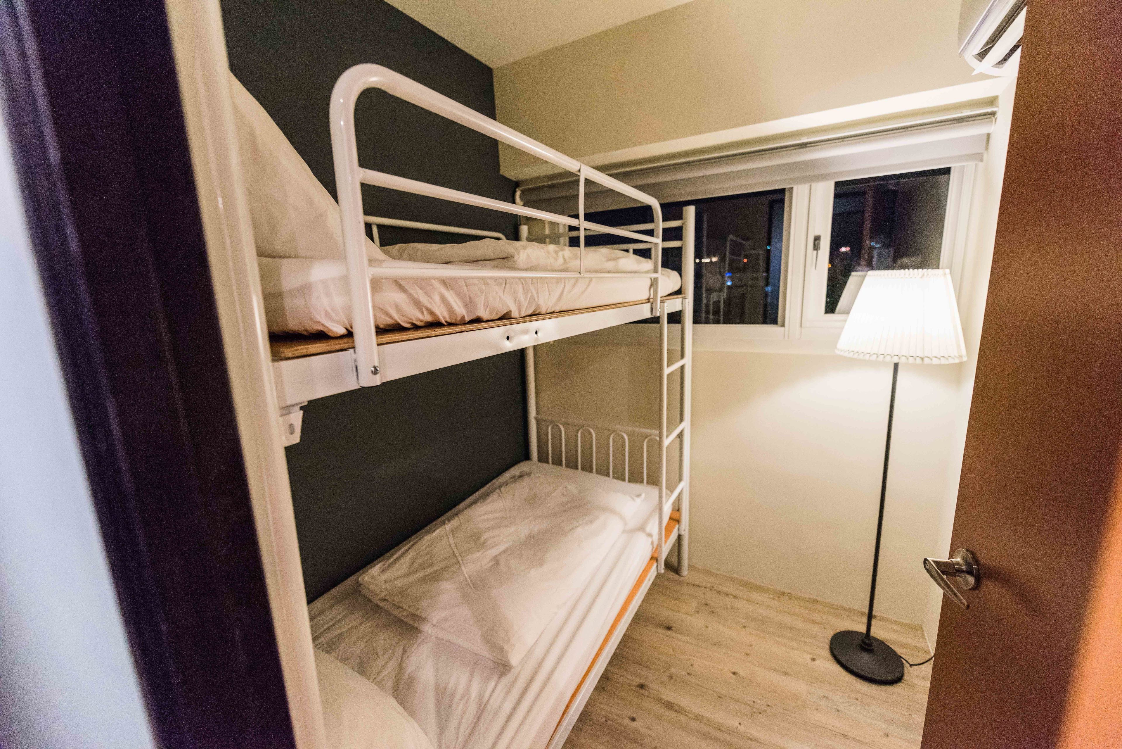 A bunk bed room with a window and a floor lamp.