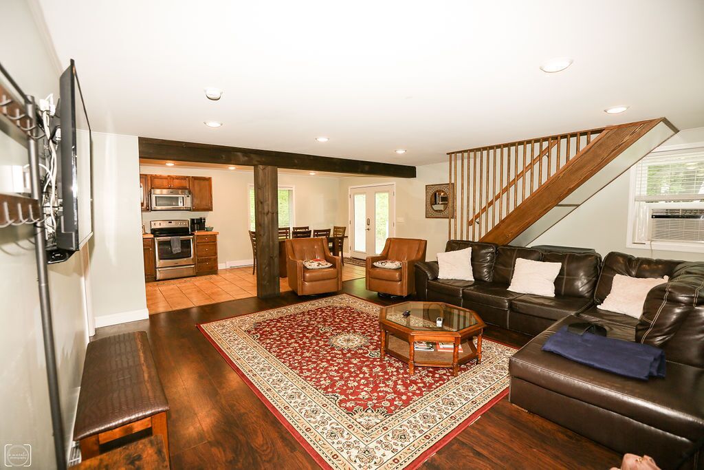 A living room with a dark brown leather sofa, a glass coffee table, and a red patterned rug. There is a staircase leading to another level.