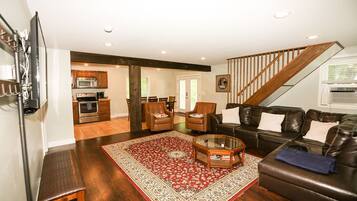 A living room with a dark brown leather sofa, a glass coffee table, and a red patterned rug. There is a staircase leading to another level.