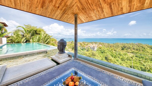 Zona junto a la piscina con vista al océano, una estatua de Buda y un frutero sobre una mesa.