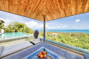 A poolside area with a view of the ocean, a Buddha statue, and a fruit bowl on a table. - Villa Jaliza (Koh Samui)