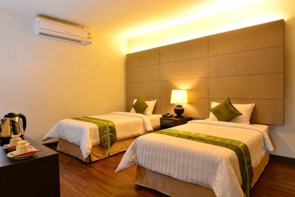 Een hotelkamer met twee bedden, een nachtkastje met een lamp en een airconditioning op de muur.