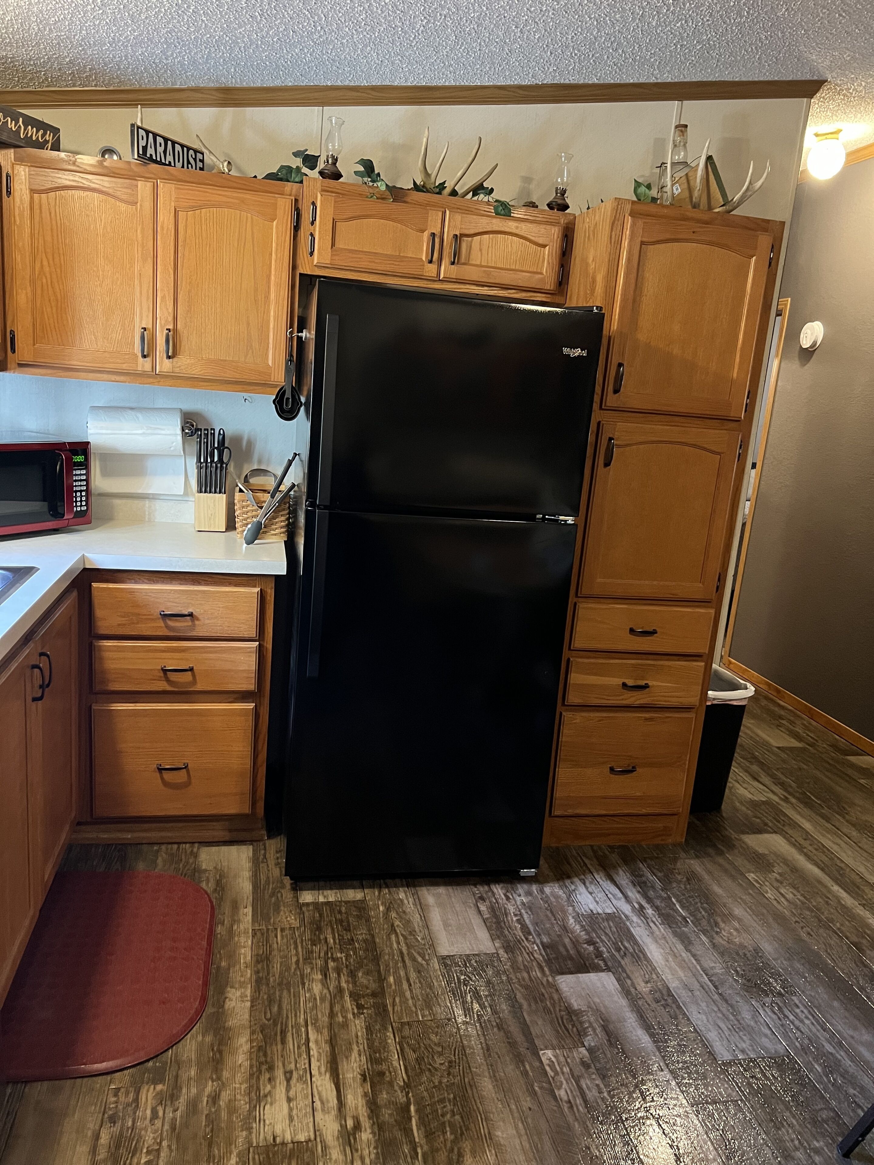 Una cocina compacta con armarios de madera, un refrigerador negro, un microondas y una pequeña zona de encimera.