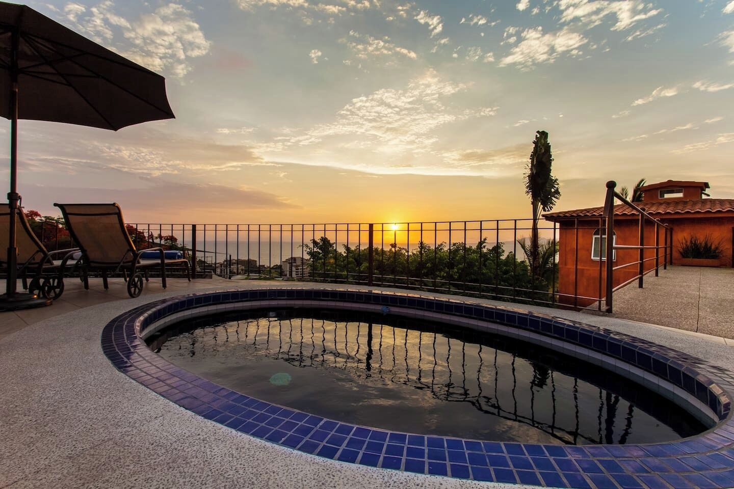 Une piscine avec des bords carrelés, des chaises longues et une vue sur le coucher de soleil.