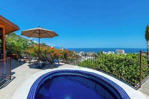 A rooftop pool with a view of the ocean, lounge chairs, and a pergola with an umbrella.
