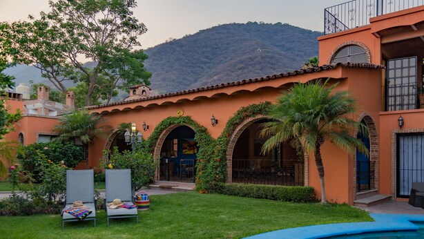 Zona de piscina con vista despejada a un edificio con arcos y una montaña al fondo.