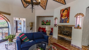 Un salón con un sofá azul, una mesa de centro de vidrio, una chimenea y una alfombra colorida.