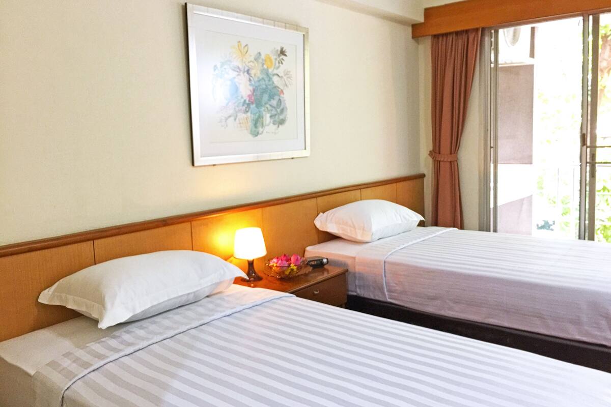 A hotel room with two beds, a nightstand with a lamp, a framed picture on the wall, and a window with curtains.