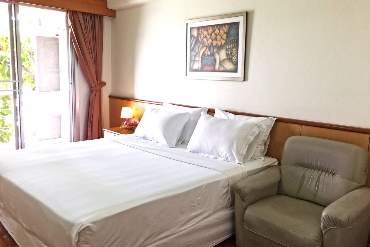 A hotel room with a large bed, a nightstand with a lamp, a chair, and a painting on the wall.