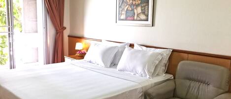 Un cuarto de hotel con una cama grande, una mesita de noche con lámpara, una silla y un cuadro en la pared.