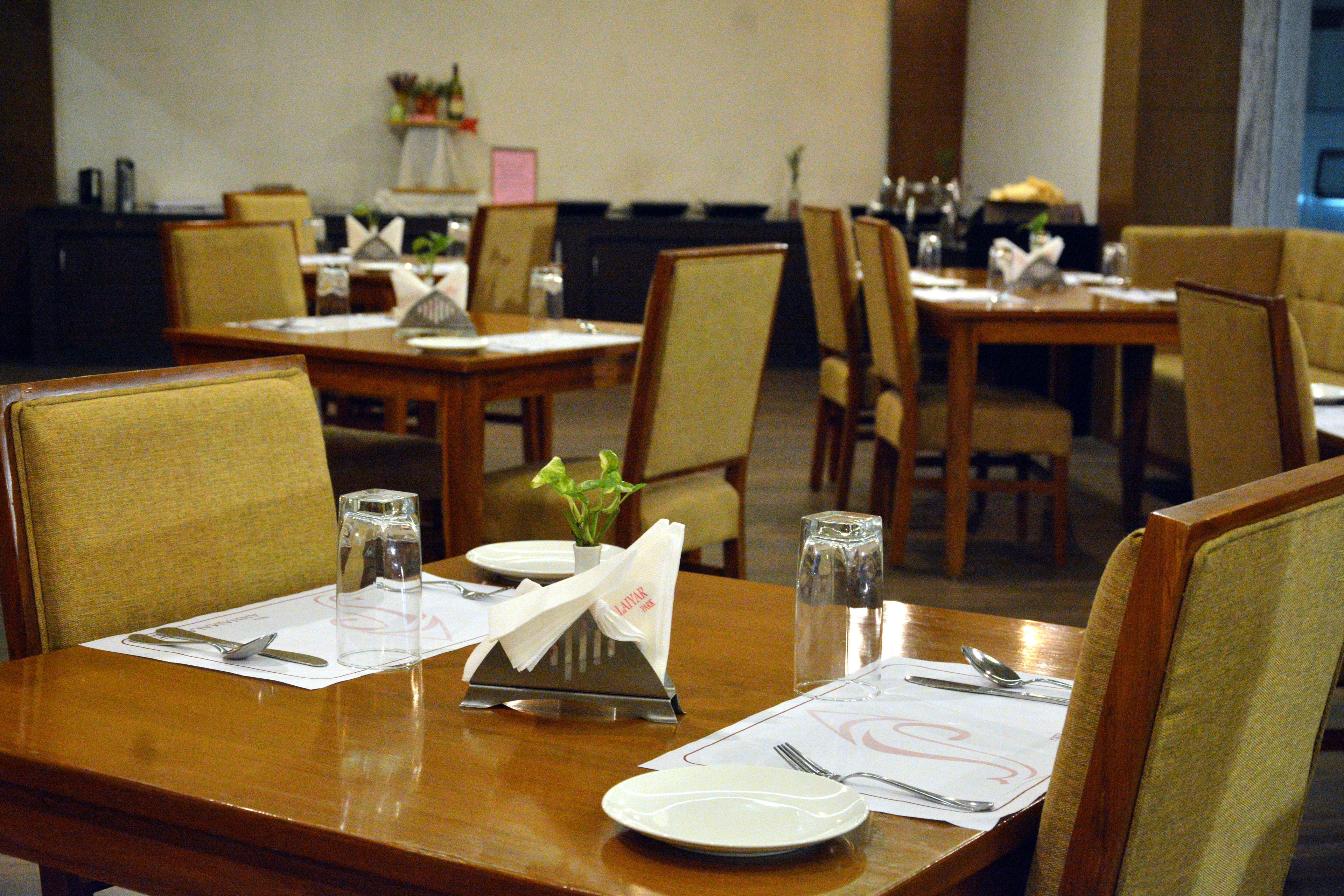 A dining area with tables set for two, each with a placemat, cutlery, and a glass of water.