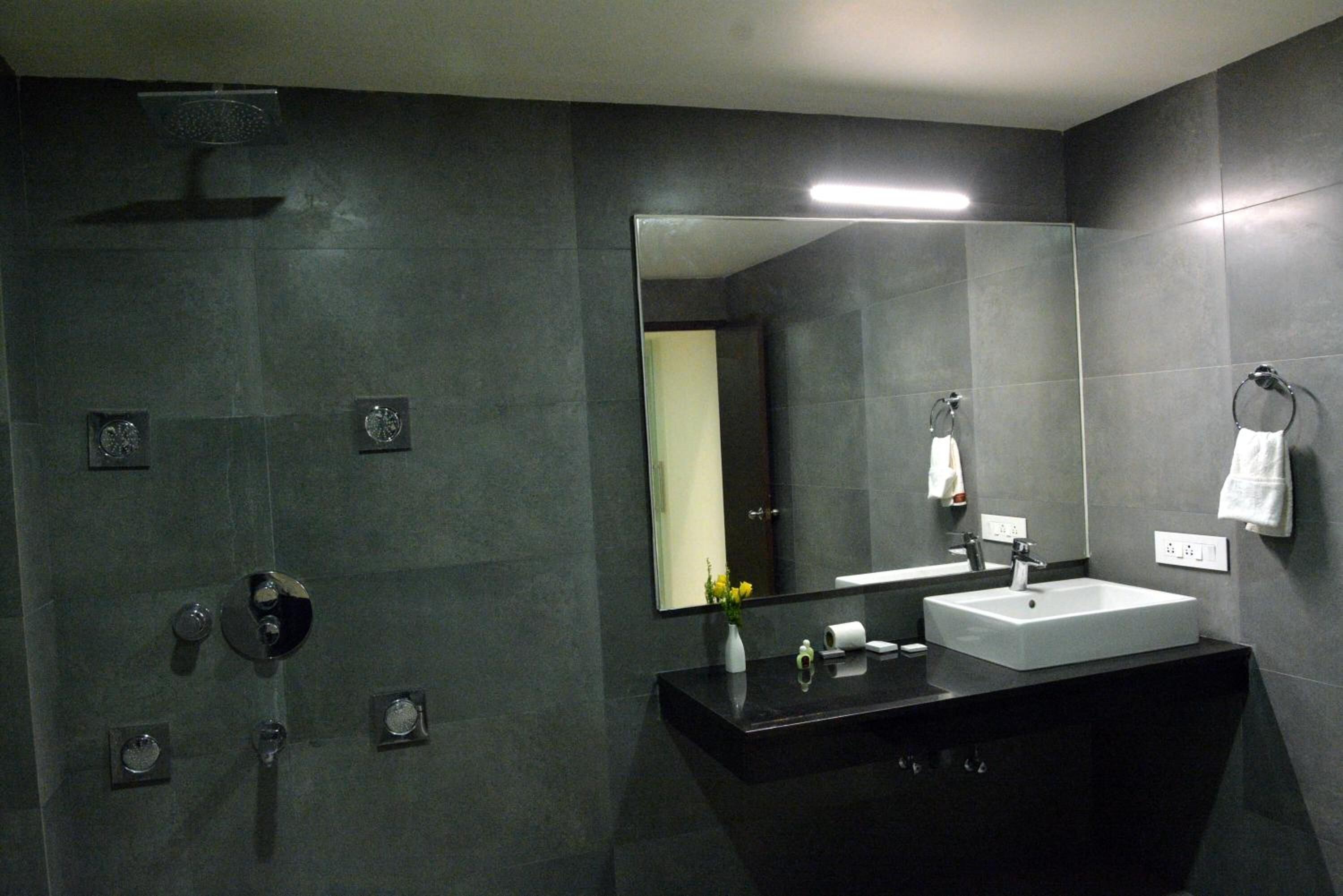 Un baño moderno con un espejo grande, una encimera negra, un lavabo blanco y un cabezal de ducha.