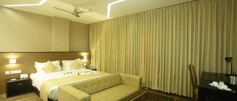 A hotel room with a bed, a sofa, a desk, and a ceiling fan.