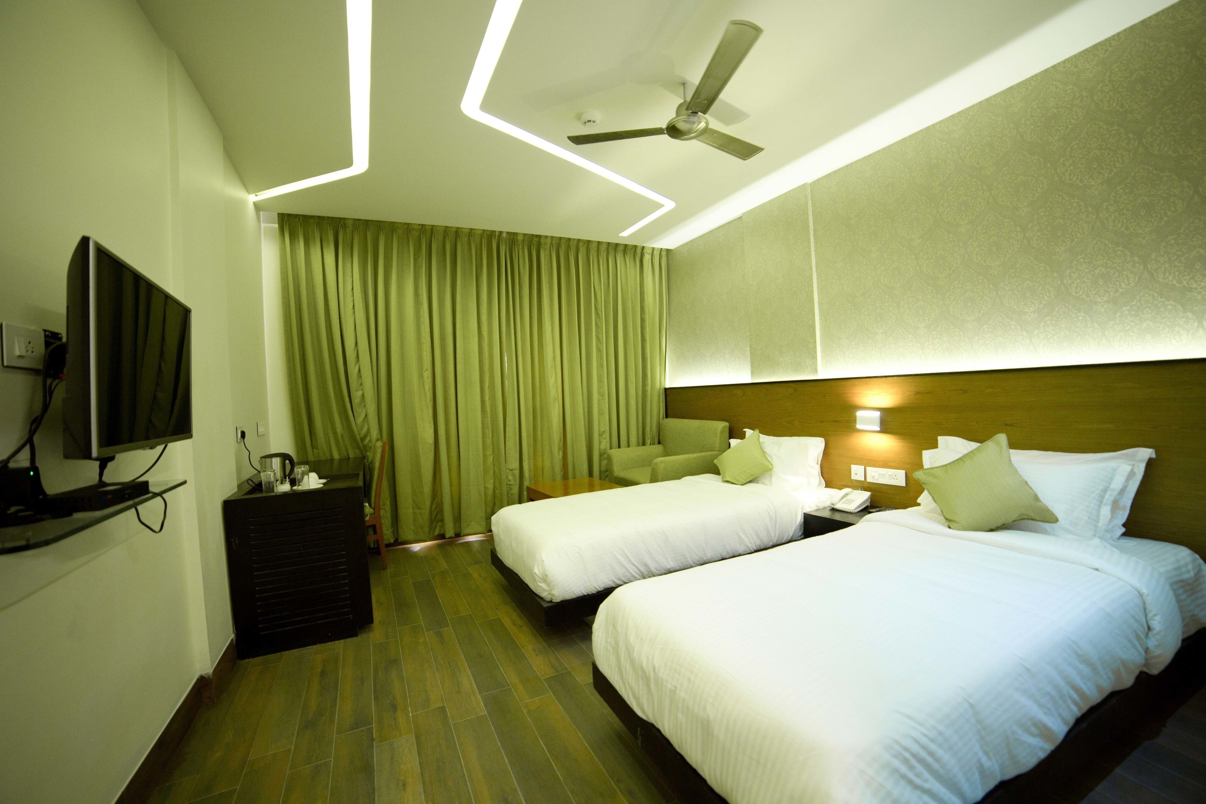 A hotel room with two beds, a ceiling fan, a TV, and a desk with a lamp.