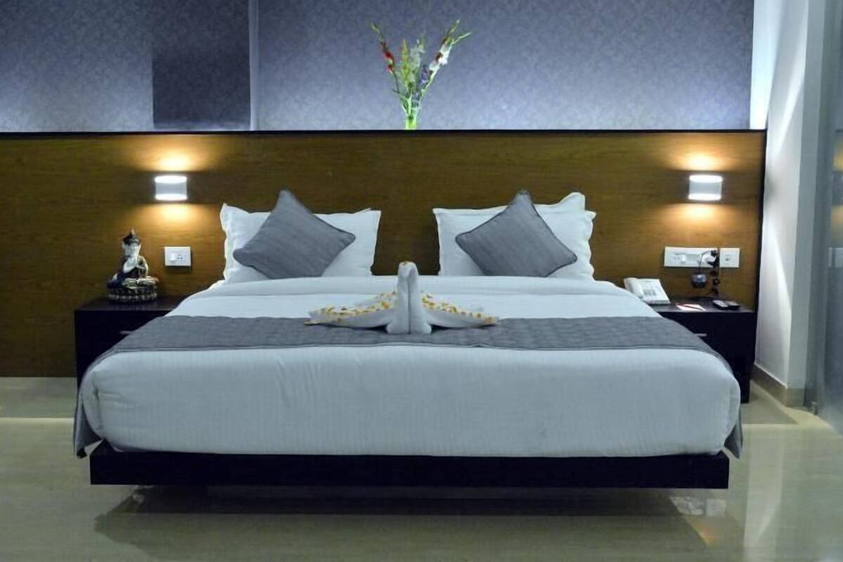 A hotel room with a large bed, two bedside tables, a nightstand, a vase with flowers, and a wall-mounted light fixture.