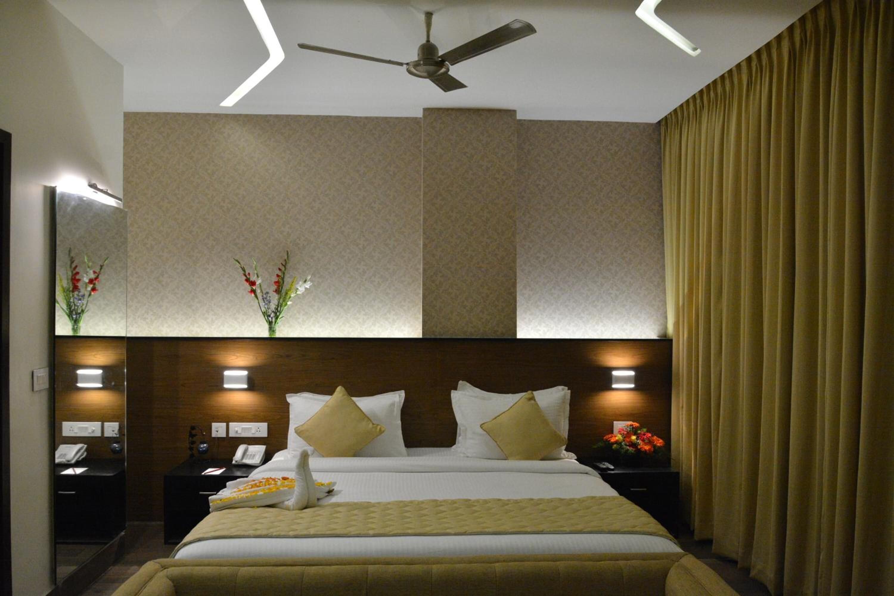 Habitación de hotel con una cama grande, un ventilador de techo, una mesita de noche con teléfono y un espejo en la pared.