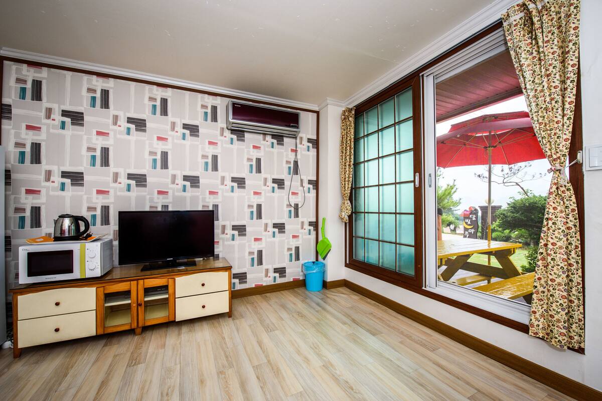 A living room with a flat-screen TV on a wooden cabinet, a microwave, and a small table with a kettle.