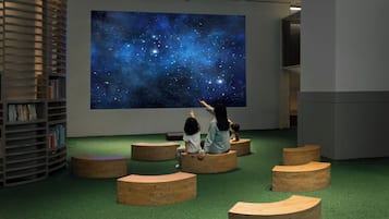 A room with a large starry sky mural, wooden circular seating, and a bookshelf.