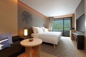 Habitación de hotel con cama, sofá, una mesa redonda con fruta, televisión y balcón con vistas.