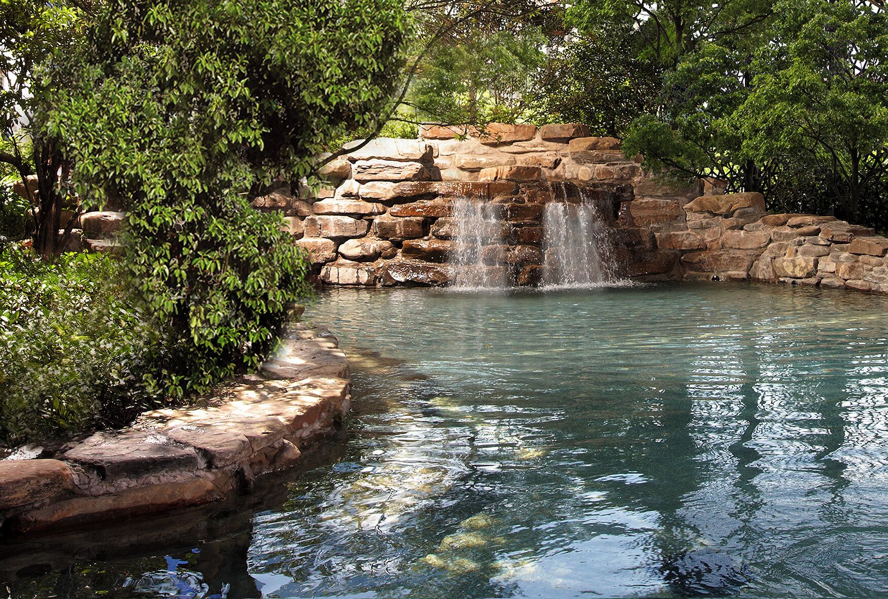 A natural water feature with a cascading waterfall, surrounded by lush greenery.