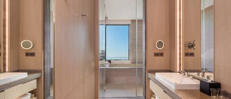 Un baño moderno con dos lavamanos, espejos grandes y vistas al cielo a través de un vidrio.