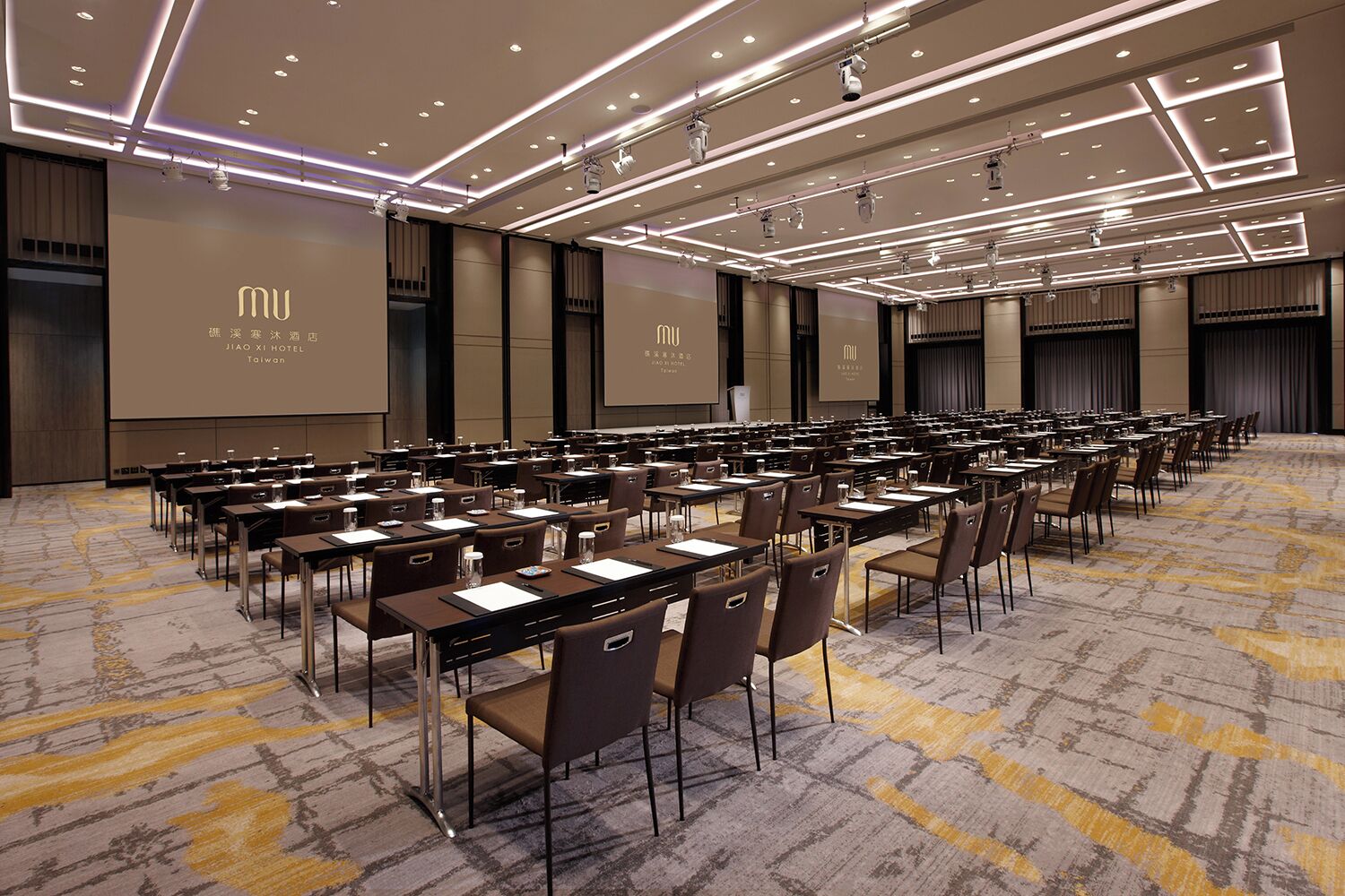 A conference room with rows of tables and chairs, equipped with microphones and projectors, at the JIAO XI HOTEL in Taiwan.