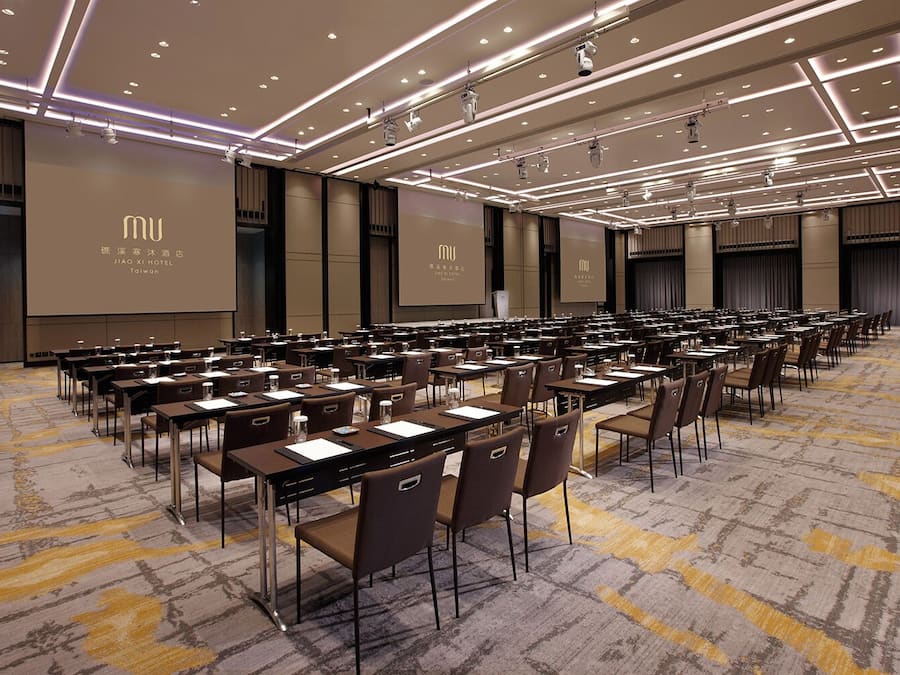 A conference room with rows of tables and chairs, equipped with microphones and projectors, at the JIAO XI HOTEL in Taiwan.