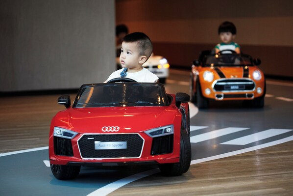Un niño manejando un coche de juguete sobre una alfombra de juegos.