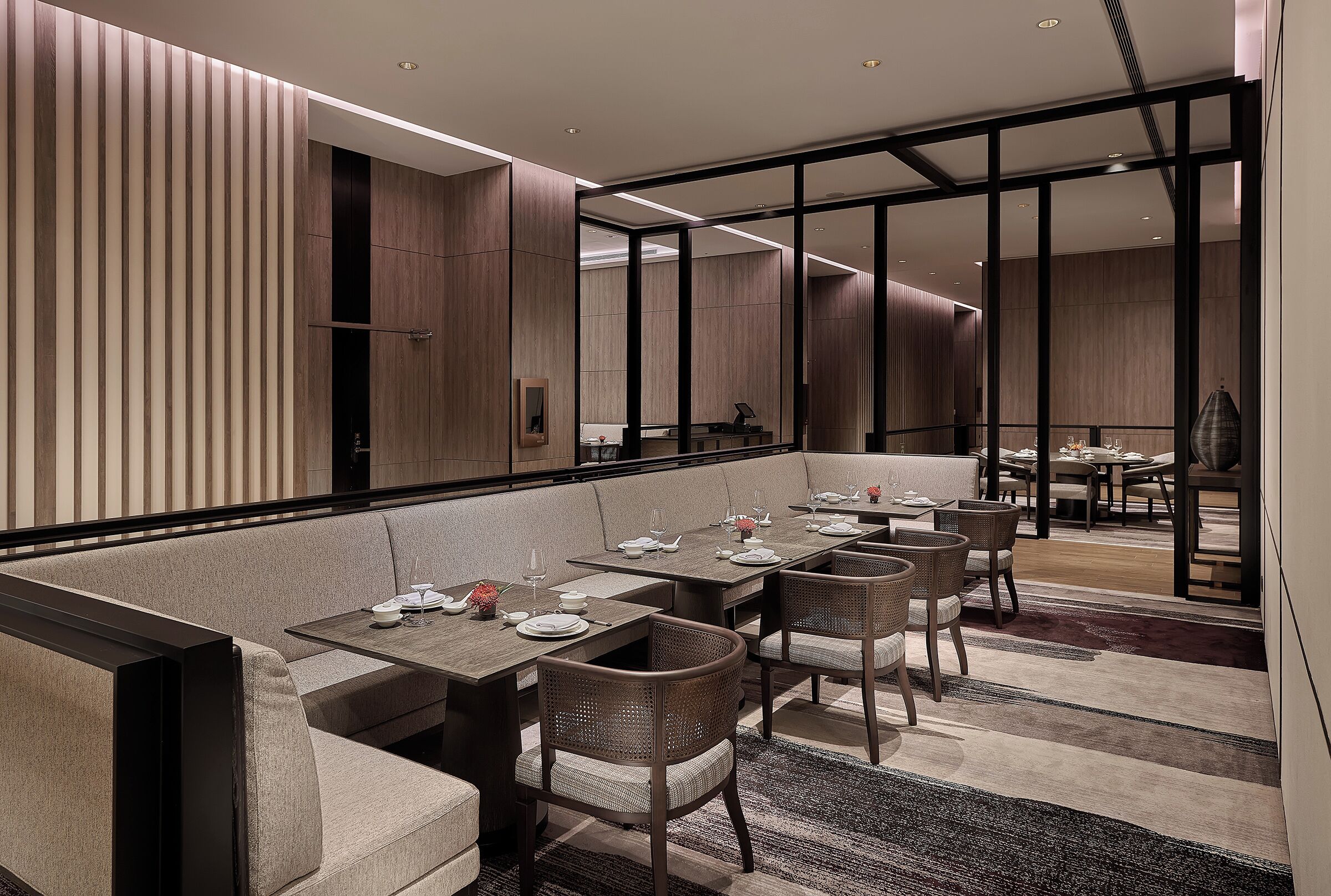 A modern dining area with a long table, cushioned seating, and a view into another room.