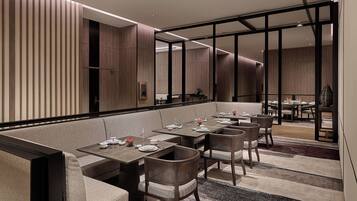 A modern dining area with a long table, cushioned seating, and a view into another room.