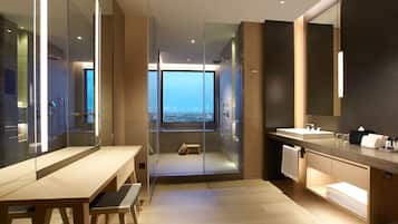 Un baño moderno con ducha envuelta en vidrio, un banco de madera, un espejo grande y vistas a la ciudad.