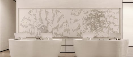 A reception area with two curved reception desks, a large abstract painting on the wall, and a wooden floor.