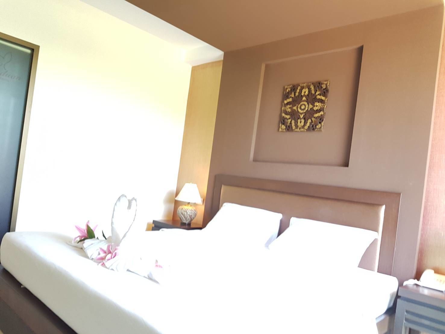A hotel room with a large bed, a nightstand with a lamp, and a wall decoration.