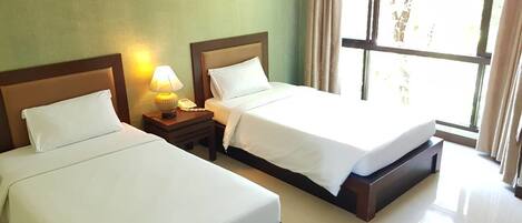 Une chambre d’hôtel avec deux lits, une table de chevet avec une lampe et une fenêtre avec des rideaux.
