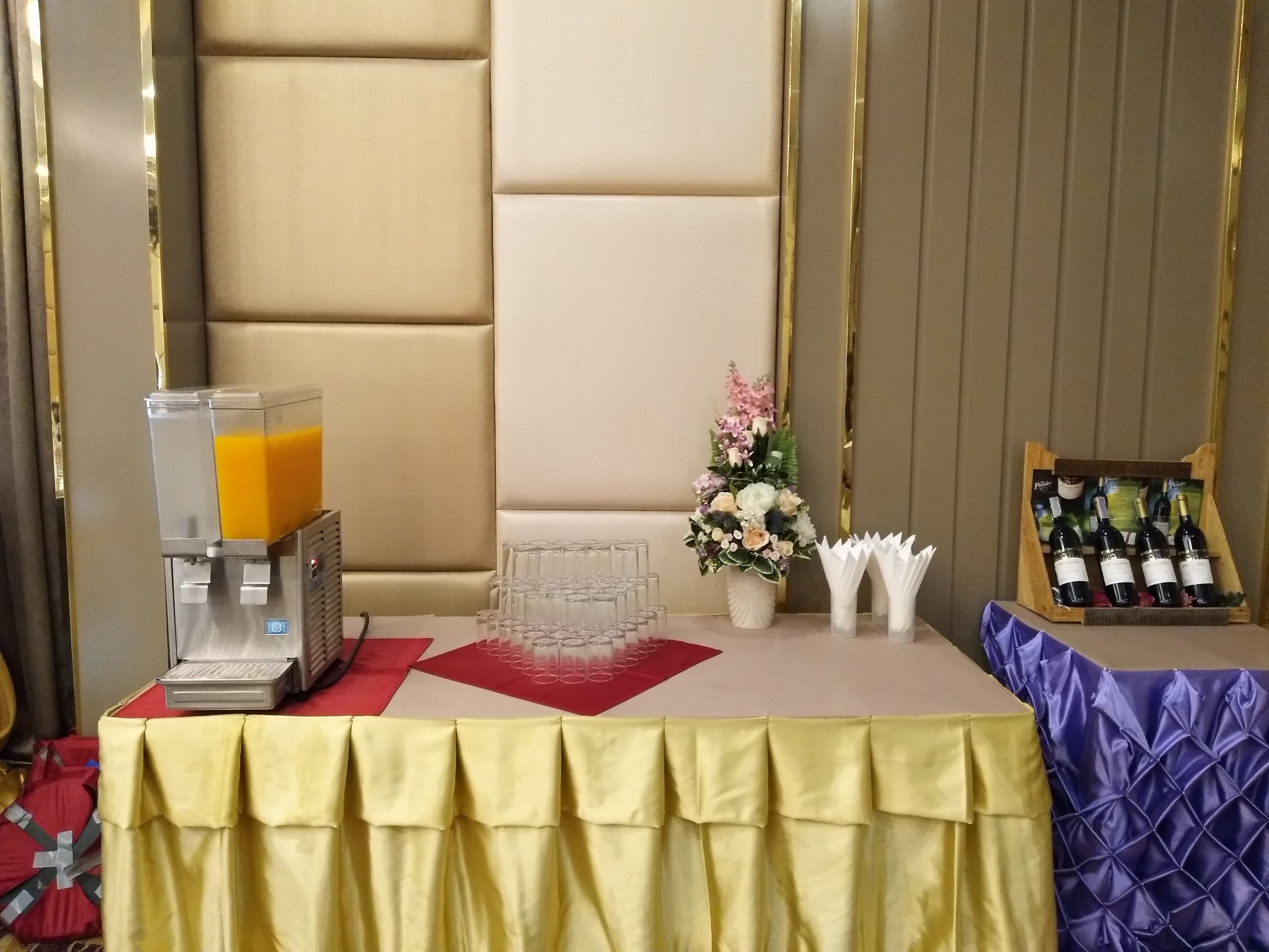 Une table avec un distributeur de jus, une composition florale et un présentoir à vin.