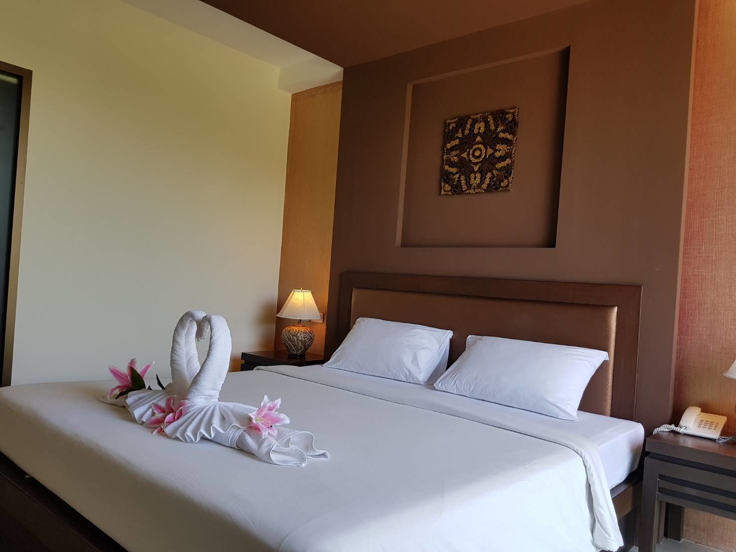 A hotel room with a neatly made bed, a bedside lamp, and a decorative wall piece.