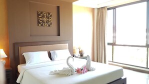 A hotel room with a large bed, a decorative wall piece, a nightstand with a lamp, and a window with curtains. - Srilamduan Hotel (Sisaket)