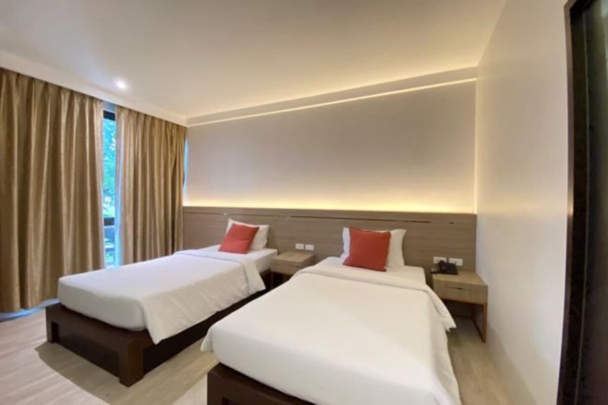 A hotel room with two single beds, a wooden headboard, a nightstand, and a large window with curtains.