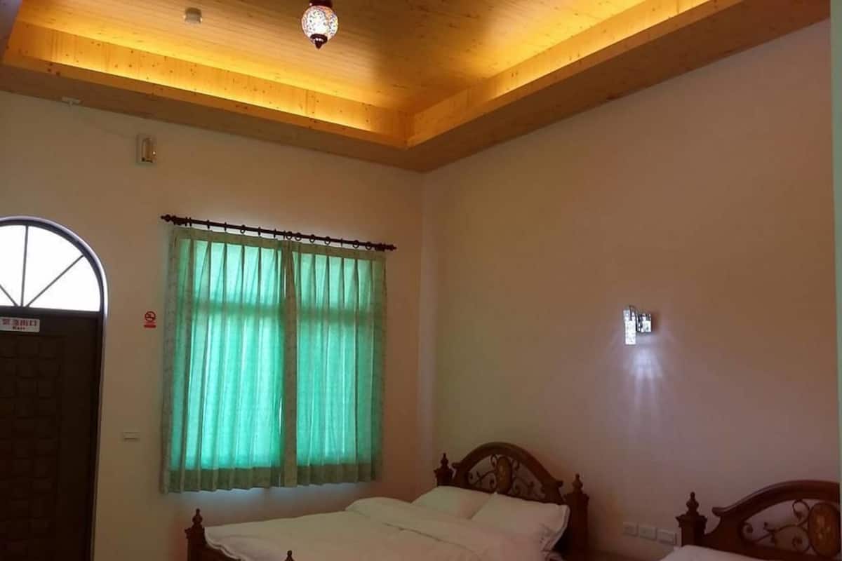 Une chambre avec deux lits en bois, une fenêtre avec des rideaux verts et un plafond en bois.