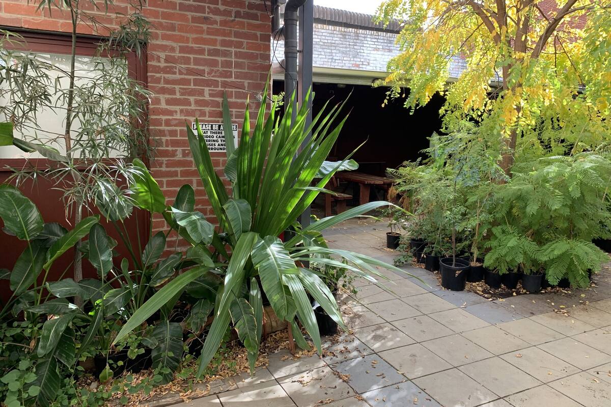 A brick building with a sign, potted plants, and a tiled patio area.