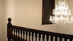 Una escalera con barandilla y balaustrada de madera, que lleva a un cuarto con un candelabro grande y ornamentado.
