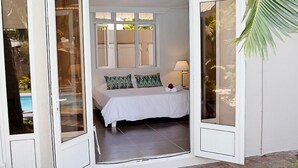 A bedroom with a bed, pillows, a lamp, and a view of a swimming pool through a glass door. - Explora Prestige (Blue Bay)