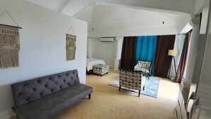 A spacious room with a grey sofa, a bed with a white headboard, a patterned chair, and a large window with curtains. - Explora Prestige (Blue Bay)