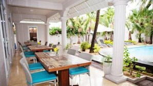A covered outdoor dining area with tables and chairs, a pool in the background, and tropical plants. - Explora Prestige (Blue Bay)