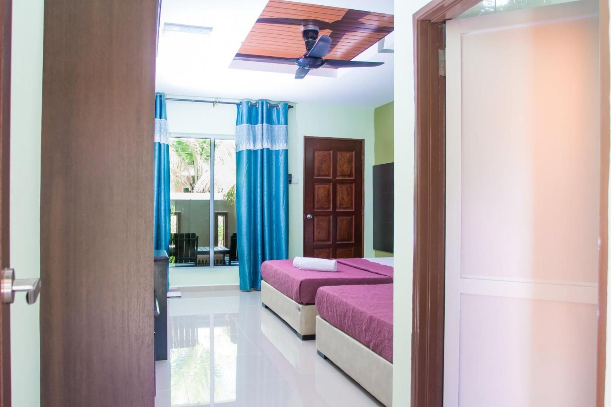 A hotel room with a bed, a door, a ceiling fan, and a view of the outside.