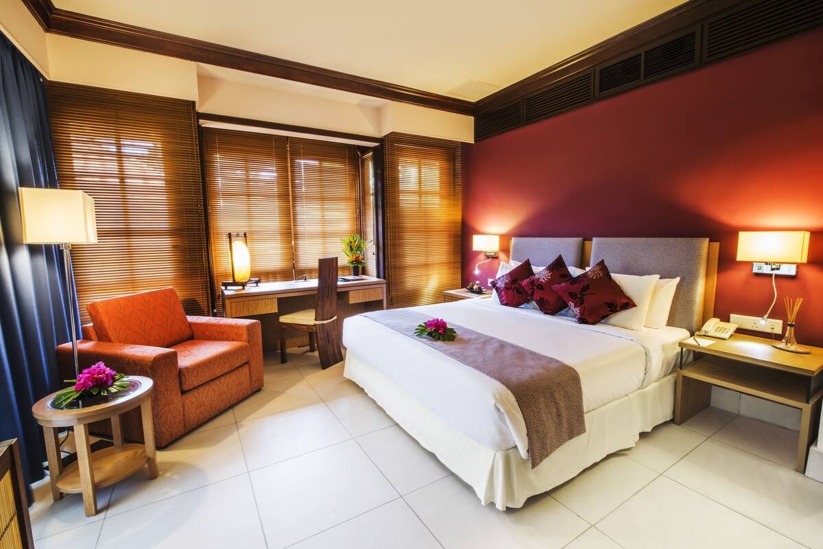 A hotel room with a large bed, a desk, a chair, and a small table with a lamp.
