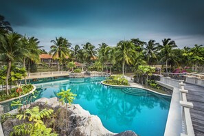 Una piscina amplia y cristalina rodeada de palmeras y una terraza de madera.