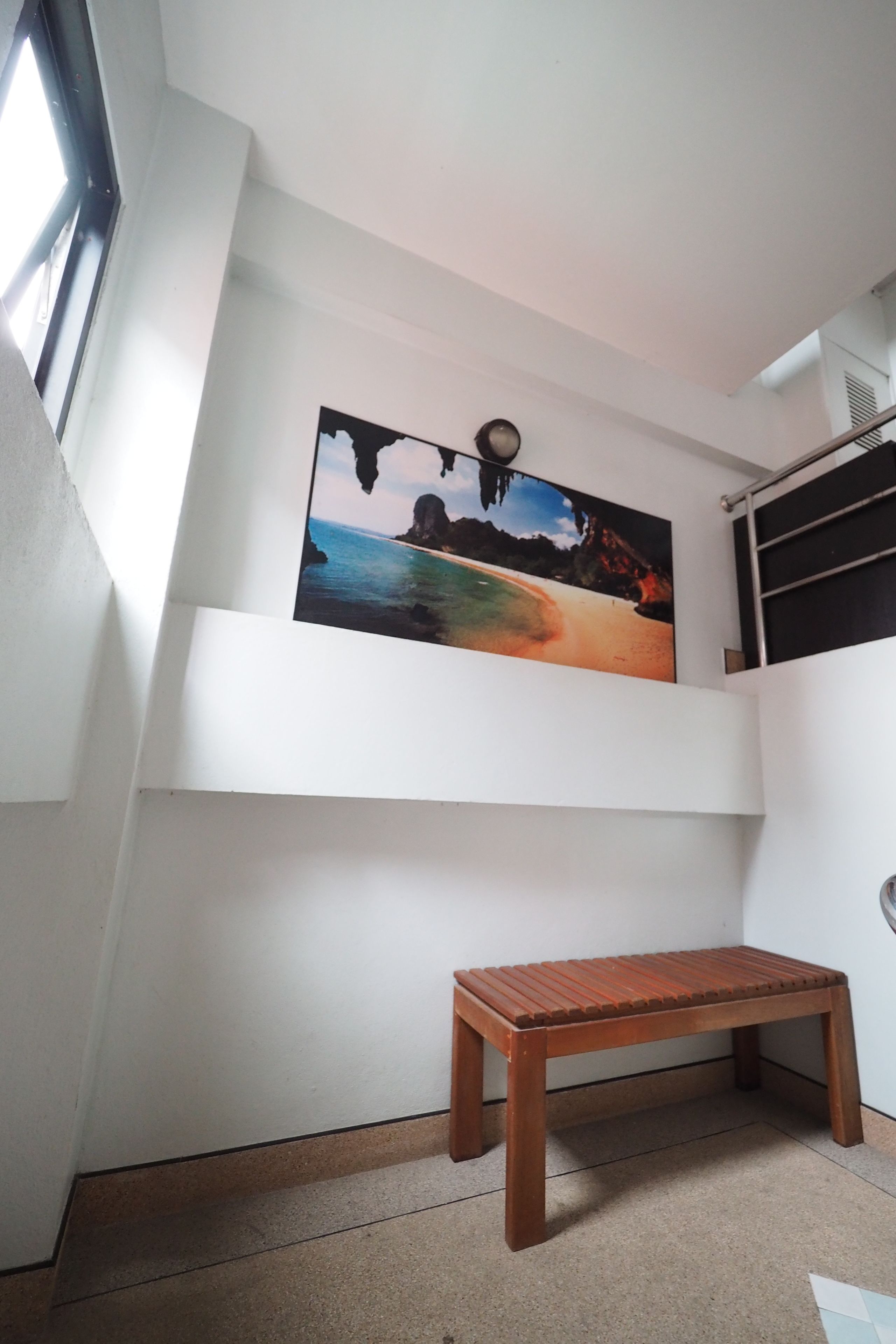 Una habitación con un banco de madera, un cuadro de una escena de playa y una ventana.